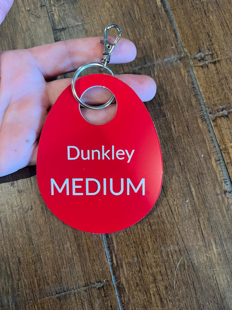 May include: Red oval-shaped keychain with a silver ring and clasp. The keychain has the text "Dunkley MEDIUM" printed in white.