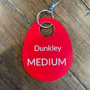 May include: Red oval-shaped key tag with a silver key ring. The tag has the text "Dunkley MEDIUM" printed in white.