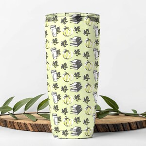 Könnte beinhalten: Ein hoher, isolierter Becher mit einem sich wiederholenden Muster aus Kürbissen, Büchern, Kaffeetassen und Blättern in Gelb-, Grau- und Weißtönen auf hellgrünem Hintergrund. Der Becher ist zylindrisch.