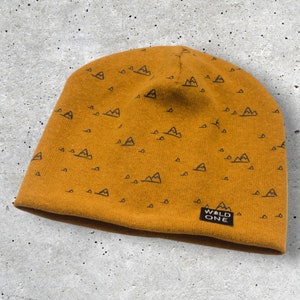 Pode incluir: Um gorro amarelo mostarda com um padrão de montanha preto e o texto "WALD ONE" no lado.
