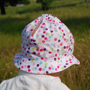 Peut inclure: Un chapeau de soleil blanc à pois multicolores. Le chapeau a une large bordure et une couronne plissée.