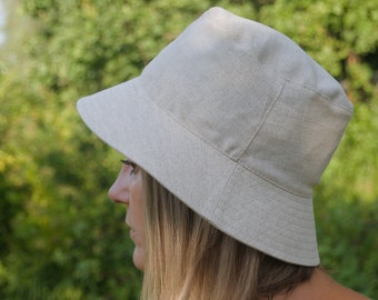 Könnte beinhalten: Ein hellbeiger, breiter Hut aus Leinen mit breiter Krempe. Der Hut ist aus einem weichen, natürlichen Stoff gefertigt und hat ein schlichtes, klassisches Design.