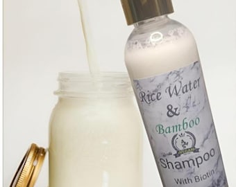 May include: A white bottle of Rice Water & Bamboo Shampoo with Biotin, labeled with a green and white logo. The bottle is 8 fl oz and is shown being poured into a clear glass jar.