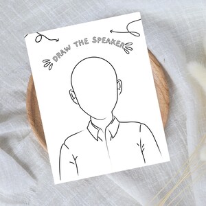 Pode incluir: Um papel branco com um desenho de contorno preto de uma pessoa sem rosto. O texto "DRAW THE SPEAKER" est&aacute; acima do desenho, com setas apontando para o desenho. O desenho est&aacute; em um prato de madeira.