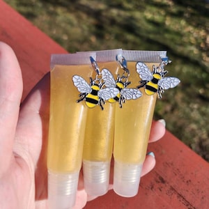 May include: Three clear tubes of honey-colored lip gloss with silver bee charms attached to the tops.