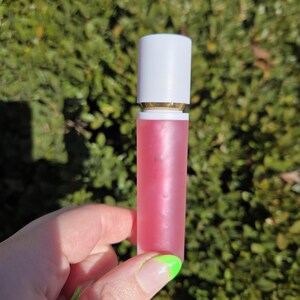 Op de afbeelding: Een transparante buis met een witte dop en een roze vloeistof erin. De buis wordt vastgehouden door een hand met groene nagellak.