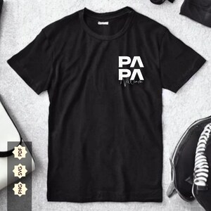 Peut inclure: T-shirt noir avec un motif graphique blanc qui dit "PA PA" avec un symbole de battement de cœur et le mot "William" en dessous.
