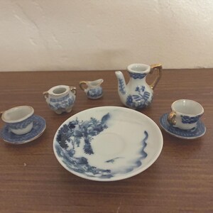 May include: A small porcelain tea set with blue and white floral patterns. The set comprises a teapot, a creamer, a sugar bowl, two cups with saucers, and a serving plate. The teapot and cups have gold detailing.