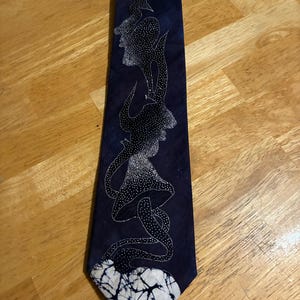 May include: A dark blue necktie featuring a white stippled graphic design of a mushroom and abstract shapes. The bottom tip of the tie displays a white and dark blue shibori-style tie-dye pattern that contrasts with the solid dark blue fabric.