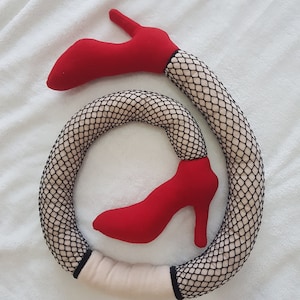 Puede incluir: Una media de red negra con un zapato de tacón alto rojo unido a cada extremo. La media está enroscada en forma de círculo.