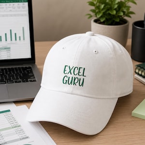 May include: White baseball cap with the text "EXCEL GURU" embroidered in green. The cap is on a desk with a laptop and papers.