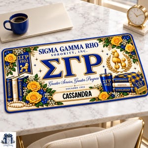 May include: A rectangular desk mat featuring the Sigma Gamma Rho Sorority, Inc. logo, the Greek letters ΣΓΡ, and the name CASSANDRA. The design includes yellow roses, blue accents, a poodle illustration, and books labeled Sisterhood, Service, and Scholarship.