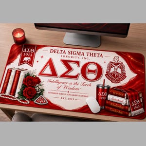 May include: A rectangular desk mat featuring Delta Sigma Theta Sorority, Inc. branding in red and white. It displays the Greek letters, the crest, an elephant emblem, red roses, a string of pearls, and a stack of books labeled with core values.