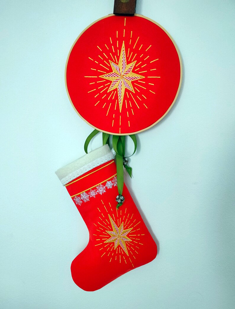 May include: A red Christmas stocking with a white lace trim and a gold star with yellow rays embroidered on it. The stocking is hanging from a red and gold hoop with a similar star design.