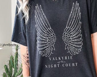 Może przedstawiać: Ciemnoszara koszulka z białym nadrukiem stylizowanych skrzydeł anioła. Poniżej skrzydeł znajduje się napis "VALKYRIE of the NIGHT COURT". Koszulka ma okrągły dekolt.