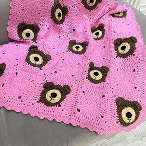 May include: A handmade crochet blanket featuring a bright pink square-based pattern with alternating solid pink squares and squares decorated with brown and beige bear faces. The blanket has a scalloped pink border along the outer edges.
