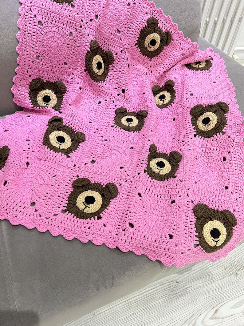 May include: A handmade crochet blanket featuring a bright pink square-based pattern with alternating solid pink squares and squares decorated with brown and beige bear faces. The blanket has a scalloped pink border along the outer edges.
