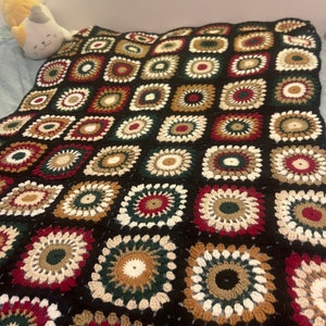 May include: A black crocheted throw blanket with a repeating pattern of colorful circles and squares. The blanket is made with a variety of yarn colors, including red, green, brown, and white.
