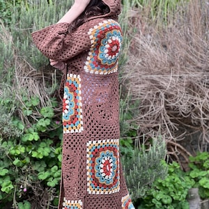 May include: A long brown crochet cardigan with a hood. The cardigan features a geometric pattern with colorful squares and circles.