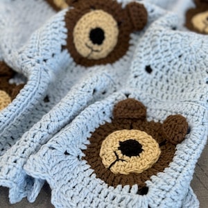 Pode incluir: Um cobertor de bebé em crochê azul claro com aplicações de urso castanho. O cobertor tem uma borda festoneada e um padrão de ponto texturizado.