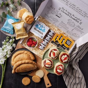 May include: A white gift box filled with a Cornish cream tea set. The box contains scones, clotted cream, jam, tea bags, and shortbread. The box is decorated with a graphic of how to enjoy a Cornish cream tea.