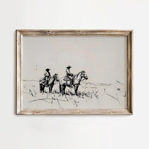 May include: A black and white line drawing of two cowboys riding horses in a field. The drawing is framed in a light wood frame.