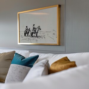 May include: A framed black and white drawing of two people on horseback in a field. The frame is gold and the drawing is set against a gray wall.