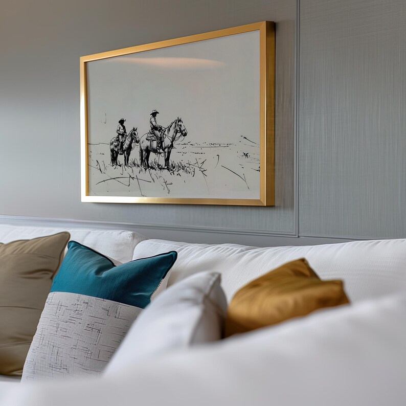May include: A framed black and white drawing of two people on horseback in a field. The frame is gold and the drawing is set against a gray wall.