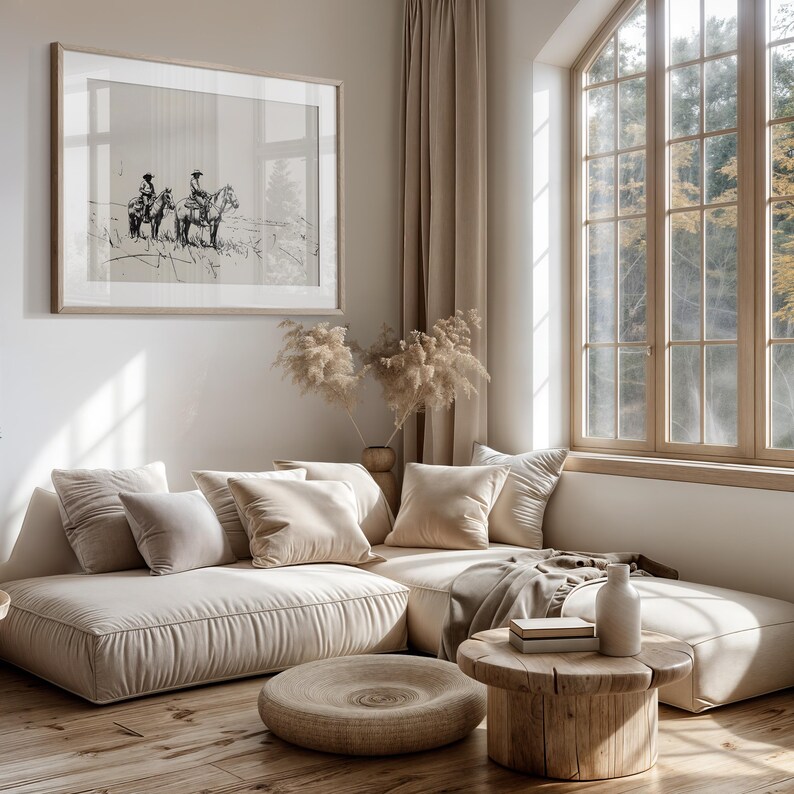 May include: A light beige sectional sofa with plush cushions and a wooden coffee table. The sofa is positioned in front of a large window with a view of trees. A black and white framed print of two people riding horses hangs on the wall.