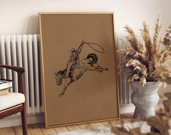 Może przedstawiać: Oprawiony wydruk z czarno-białą ilustracją kowboja na dzikim koniu. Kowboj trzyma lasso, a koń skacze. Wydruk ma brązowe tło i drewnianą ramę, idealny do rustykalnych wnętrz.