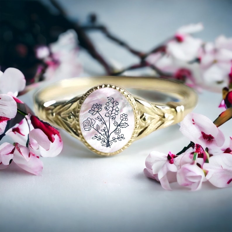 May include: A gold ring with a white oval cameo featuring a black line drawing of a bouquet of flowers.