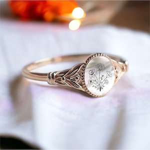 May include: A gold ring with a white oval cameo featuring a black line drawing of a bouquet of flowers.