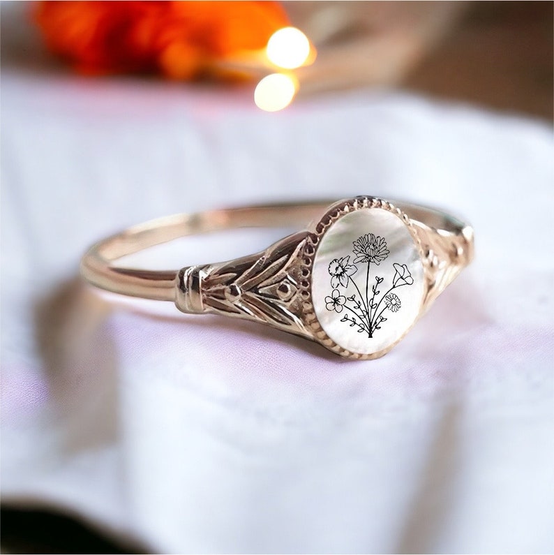 May include: A gold ring with a white oval cameo featuring a black line drawing of a bouquet of flowers.