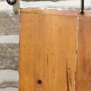 May include: A wooden sign with a natural wood finish. The sign is made of two pieces of wood that are joined together. The wood has a knot in the center and a few other knots around the edges.
