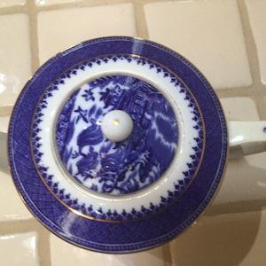 以下が含まれることがあります： 青と白の磁器ティーポット、蓋付き。 蓋には白いノブが付いた中央のデザインがあり、青と白の模様で囲まれています。 ティーポットには白いハンドルと注ぎ口があり、タイルの表面に置かれています。