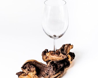 Puede incluir: Una copa de vino transparente se sienta sobre un trozo de madera a la deriva. La madera a la deriva es marrón y tiene un aspecto natural y desgastado.