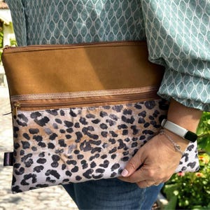 Peut inclure: Une pochette zippée à deux compartiments, de couleur marron et à imprimé léopard. La pochette est fabriquée dans un tissu doux et résistant et se ferme par une fermeture éclair.