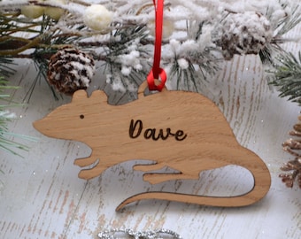 May include: A wooden rat Christmas ornament with the name "Dave" engraved on it. The ornament is hanging from a red ribbon.