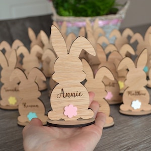 May include: A set of wooden bunny place card holders with personalised names. Each bunny is painted with a different coloured flower on the bottom. The names include Annie, Matthew, Vivian, and Regan.