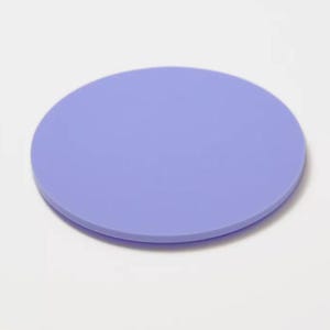 May include: A solid, round coaster in a soft periwinkle color. The coaster is made of a smooth material and is designed to protect surfaces from drink condensation. The simple design makes it suitable for various home decor styles.