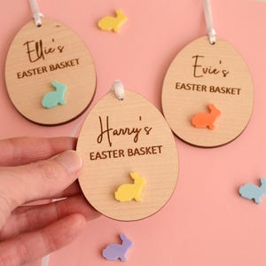 May include: Three wooden Easter egg-shaped ornaments with bunny cutouts and personalised names. The ornaments read "Ellie's Easter Basket", "Evie's Easter Basket", and "Harry's Easter Basket".