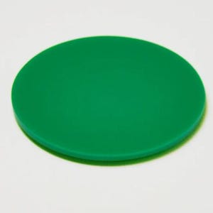 May include: A solid green, circular object, possibly a coaster or lid, is centered in the frame. The object has a smooth surface and a slightly rounded edge. The background is a plain white.