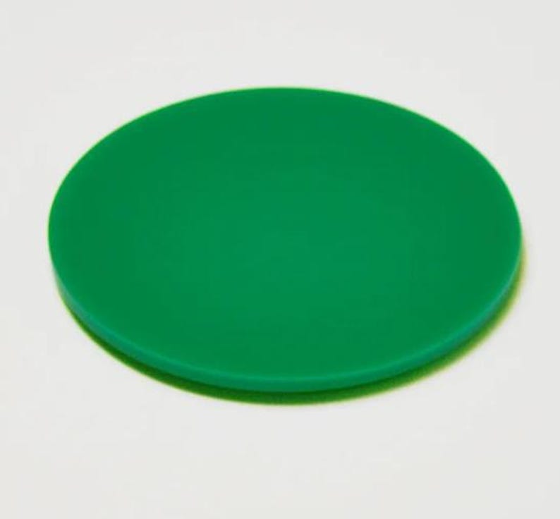 May include: A solid green, circular object, possibly a coaster or lid, is centered in the frame. The object has a smooth surface and a slightly rounded edge. The background is a plain white.