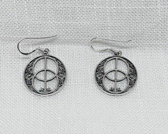 May include: A pair of silver earrings. Each earring has a circular design with a detailed pattern around the edge and a central geometric shape. The earrings have a hook closure.