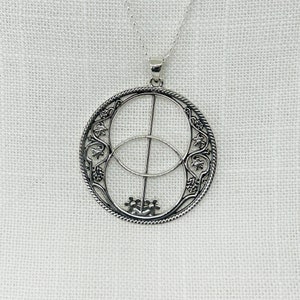 Peut inclure: Un collier avec un pendentif en argent en forme de cercle avec deux cercles qui se chevauchent et une ligne verticale au centre. Les cercles sont décorés de motifs floraux complexes.