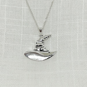 Peut inclure: Un collier en argent avec un pendentif en forme de chapeau de sorcier avec des étoiles.