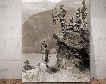 May include: A black and white photograph of five Native American men standing on a rocky cliff overlooking a lake. The men are wearing traditional clothing and headdresses. One man is holding a staff with feathers. The background is a mountain range.