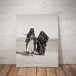 Puede incluir: Fotografía en blanco y negro de dos personas con vestimenta beduina tradicional. Una persona lleva un objeto largo sobre el hombro. La imagen se titula "109. Bedouin Sweethearts."