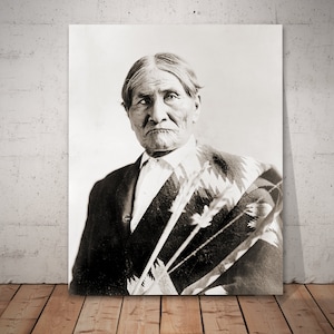 May include: Black and white portrait photograph of an older Native American man wearing a traditional blanket. He is looking directly at the camera with a serious expression.