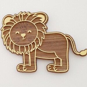 May include: A wooden lion-shaped decoration with a smiling face. The lion has a brown body and a light brown mane and outline. The lion is a cute, cartoon-like design.